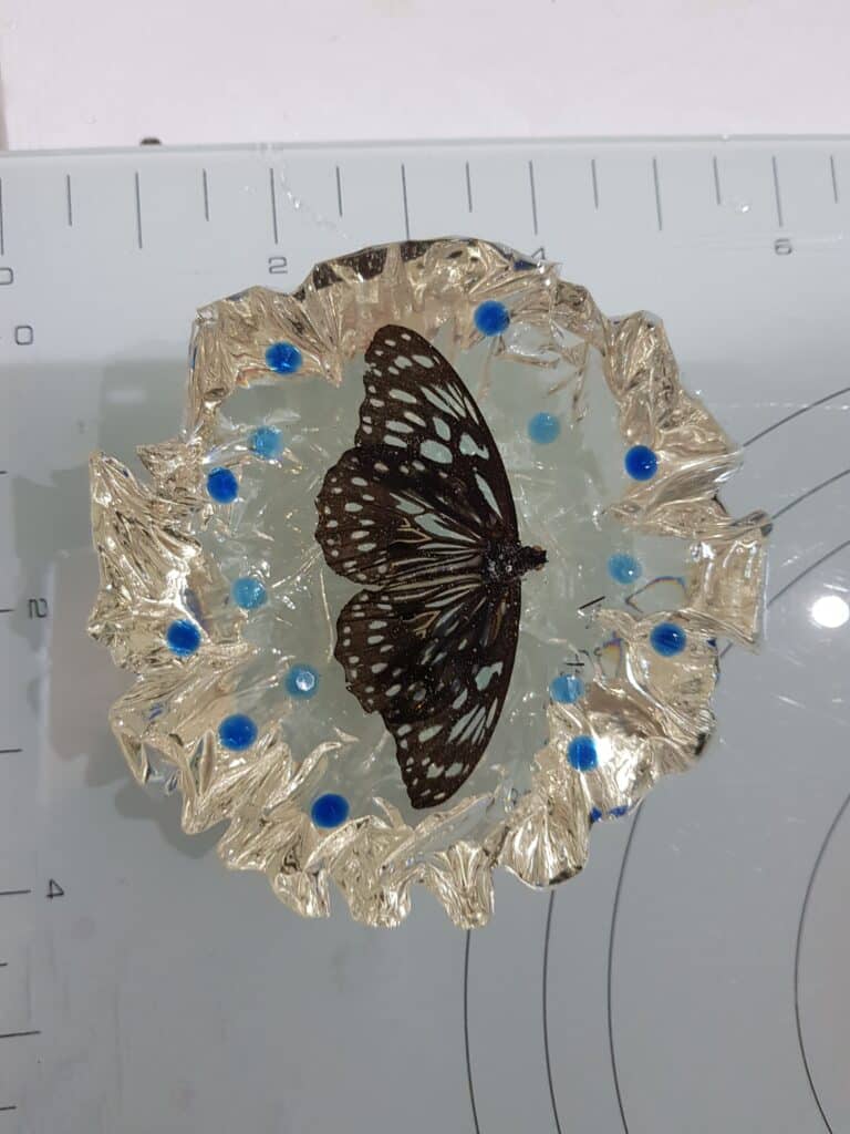 Resin Piece An resin art piece featuring a black and white butterfly embedded within clear resin, adorned with silver edges and blue beads.